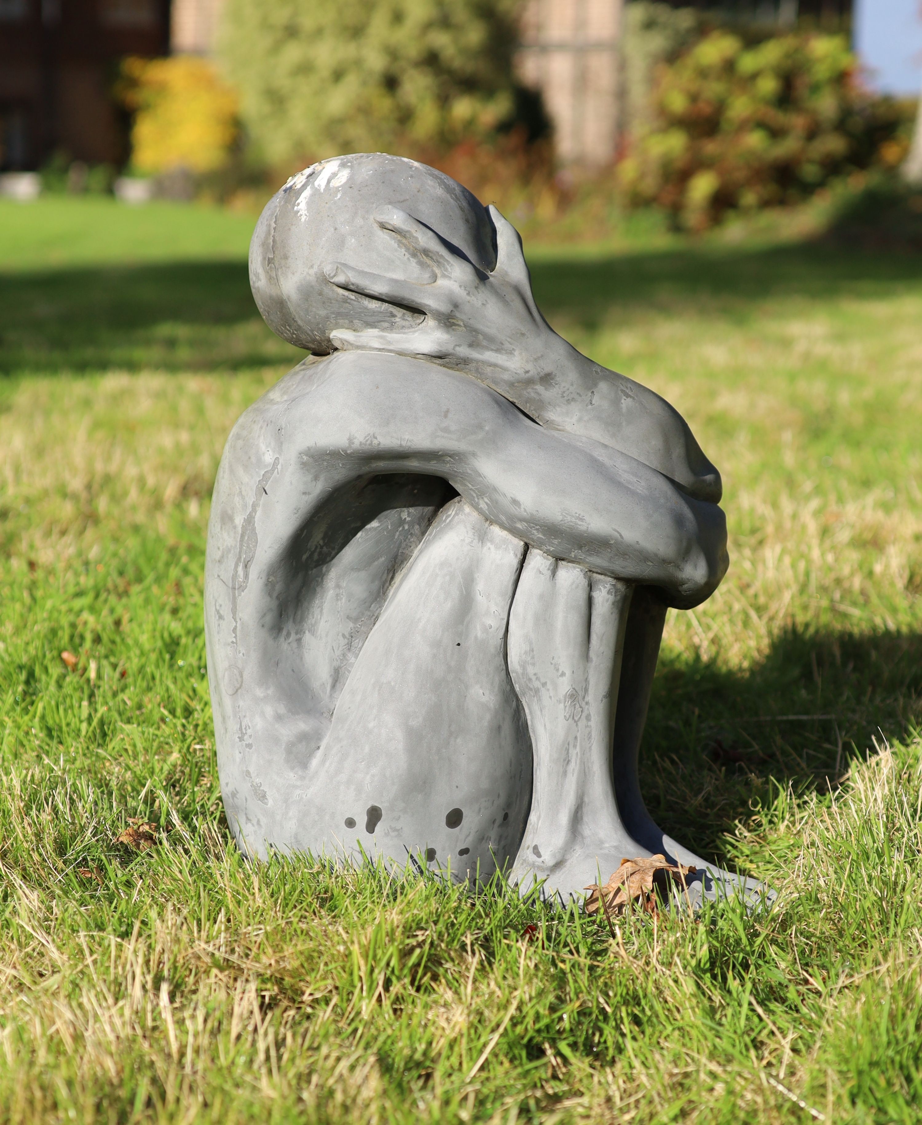 A simulated lead resin garden statue of a seated man, height 49cm, with a damaged marble pedestal, height 78cm